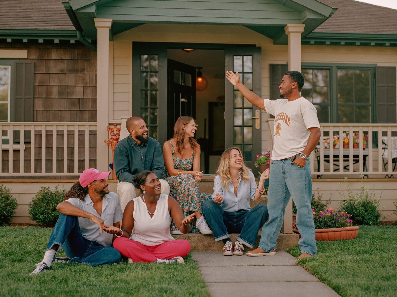 Friends laughing together on the front steps of a welcoming house at sunset, one of them waving hello